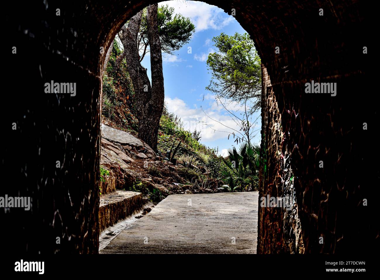 View from inside a tunnel to a green landscape with trees and blue sky. Passage to a beach Stock Photo
