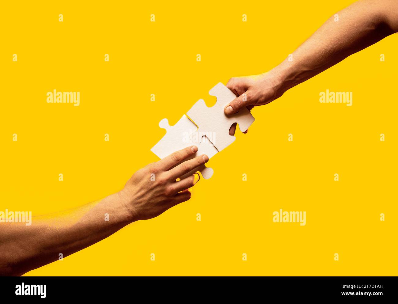Two hands trying to connect couple puzzle piece on yellow background ...