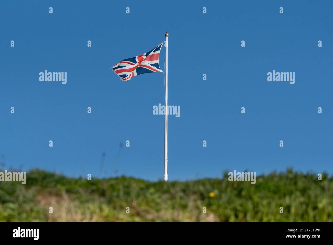 The Union Flag Union Jack flying from a flagpole against a blue sky in