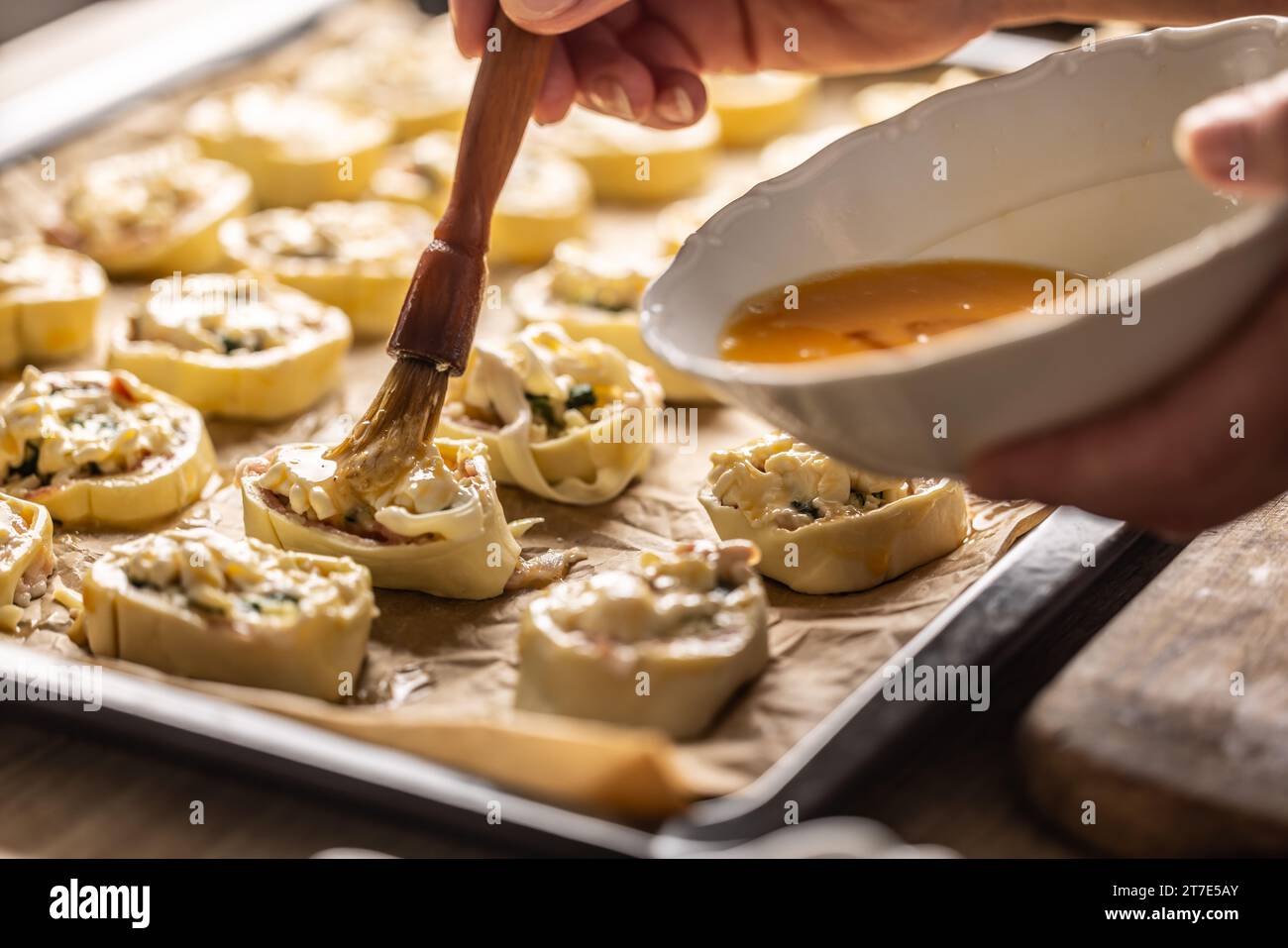 The cook brushes an egg onto a puff pastry roll. Recipe procedure 9 of
