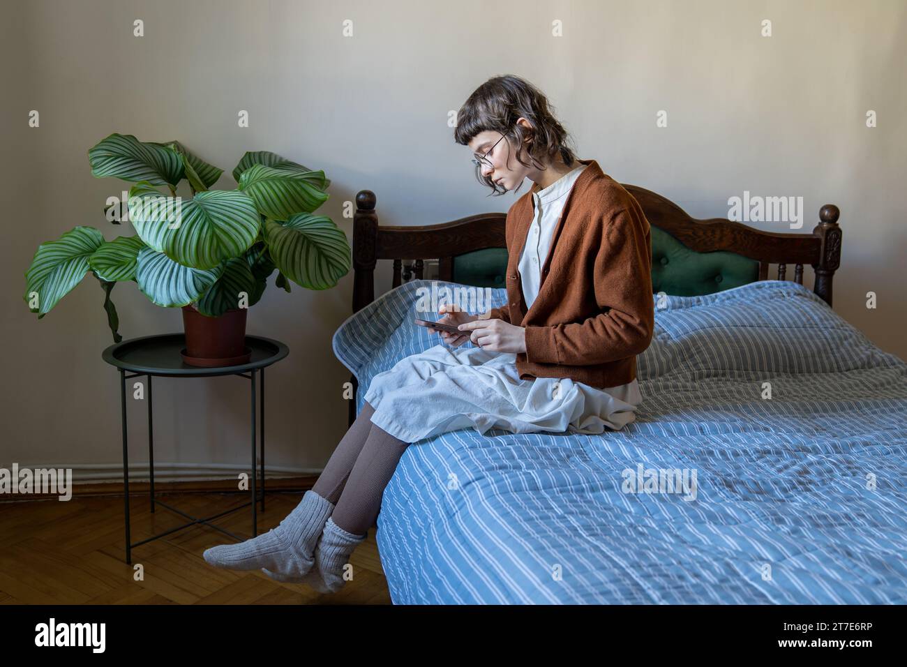 Unsociable teen girl sitting on bed with smartphone, scrolling, feeling lonely, rejected, unhappy Stock Photo