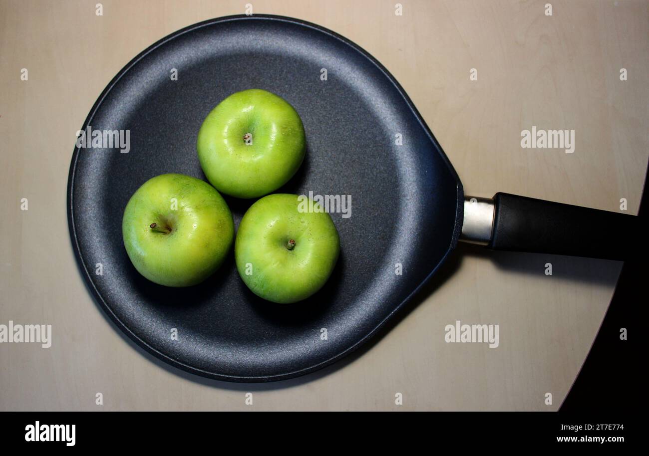 Three ripe green juicy apples in a frying pan on wooden table Stock Photo