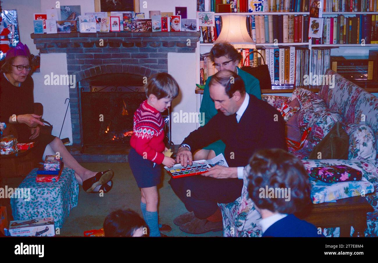 Father and son with Christmas present on Christmas Day in the 1960s. Grandparents and mother looking on. Many Christmas presents open and wrapped in view and Christmas cards. A real fire in the background. Northamptonshire England 1968 Stock Photo