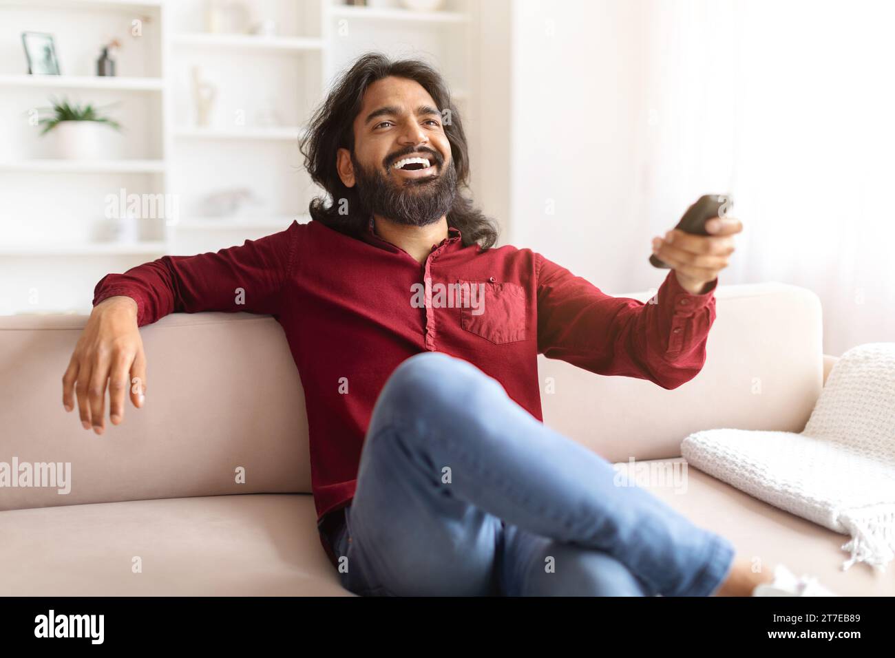 Emotional indian man watching TV at home, laughing Stock Photo
