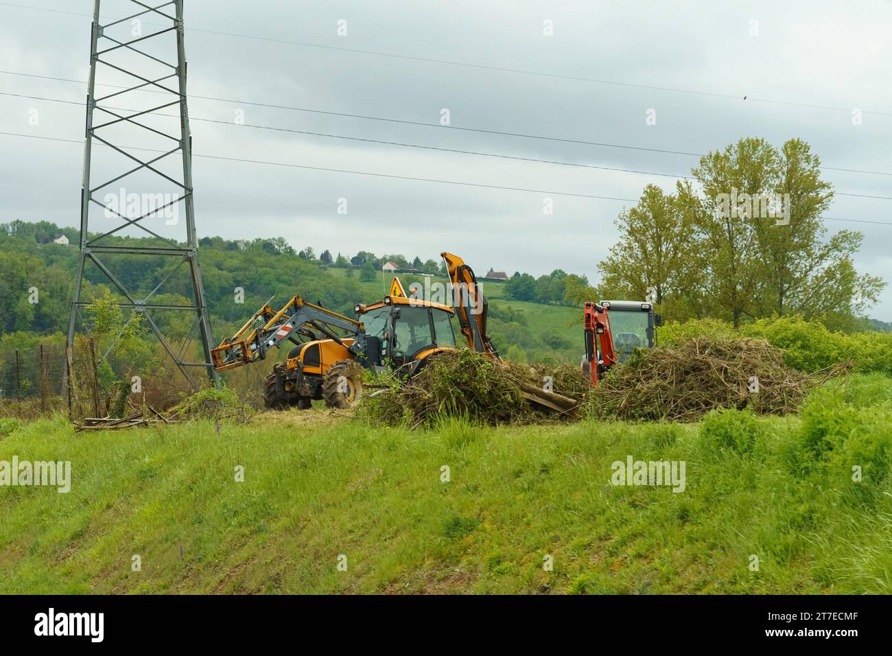 Tractors with brush cutters stand along the road on a hill behind cut bushes. Roadside maintenance. Stock Photo