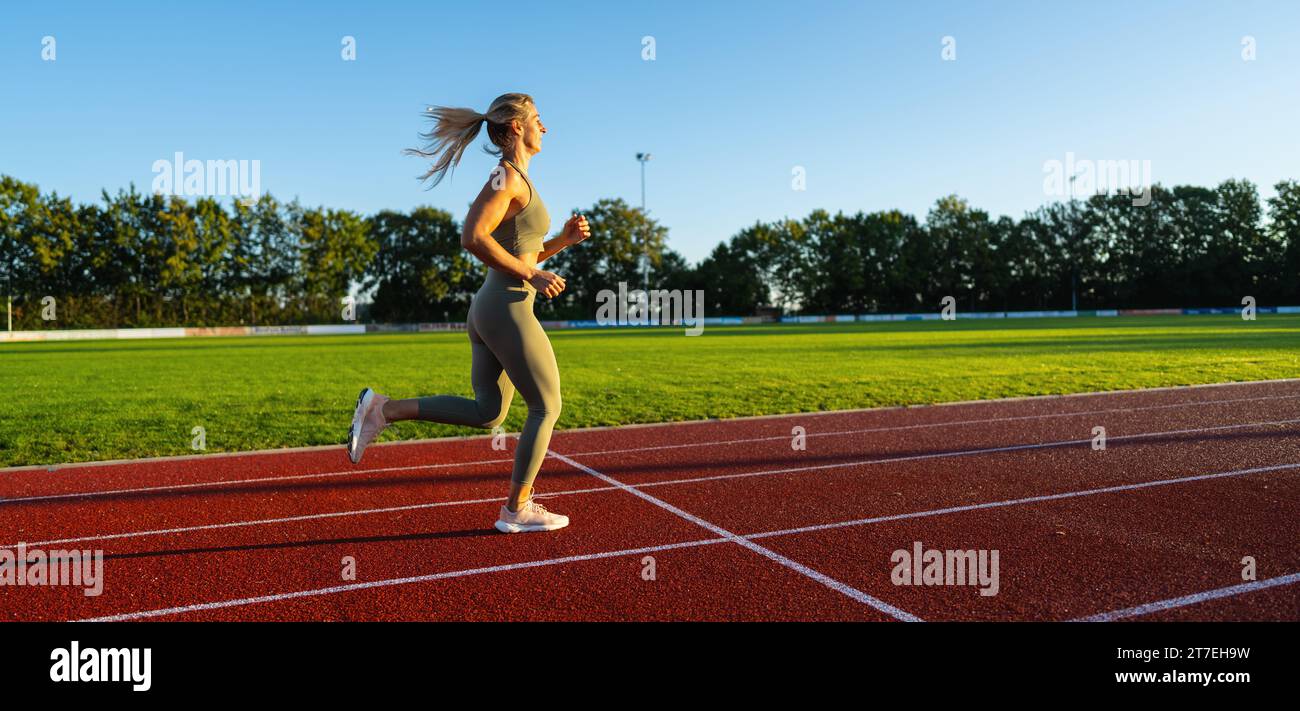 Female athlete running on a sunny track field Stock Photo