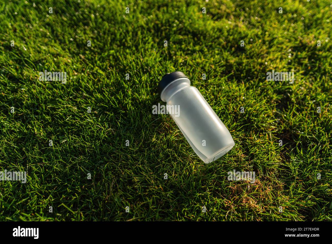 Water bottle lying on the grass in sunlight. Sports gear concept image Stock Photo