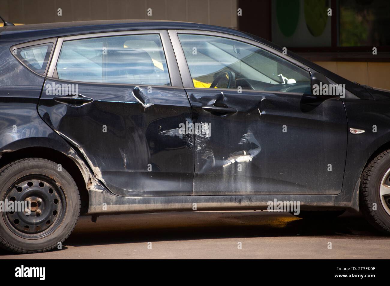 Car is viewed from side. Dent on car. Scratches in vehicles. Details of damage after accident. Black transport. Stock Photo