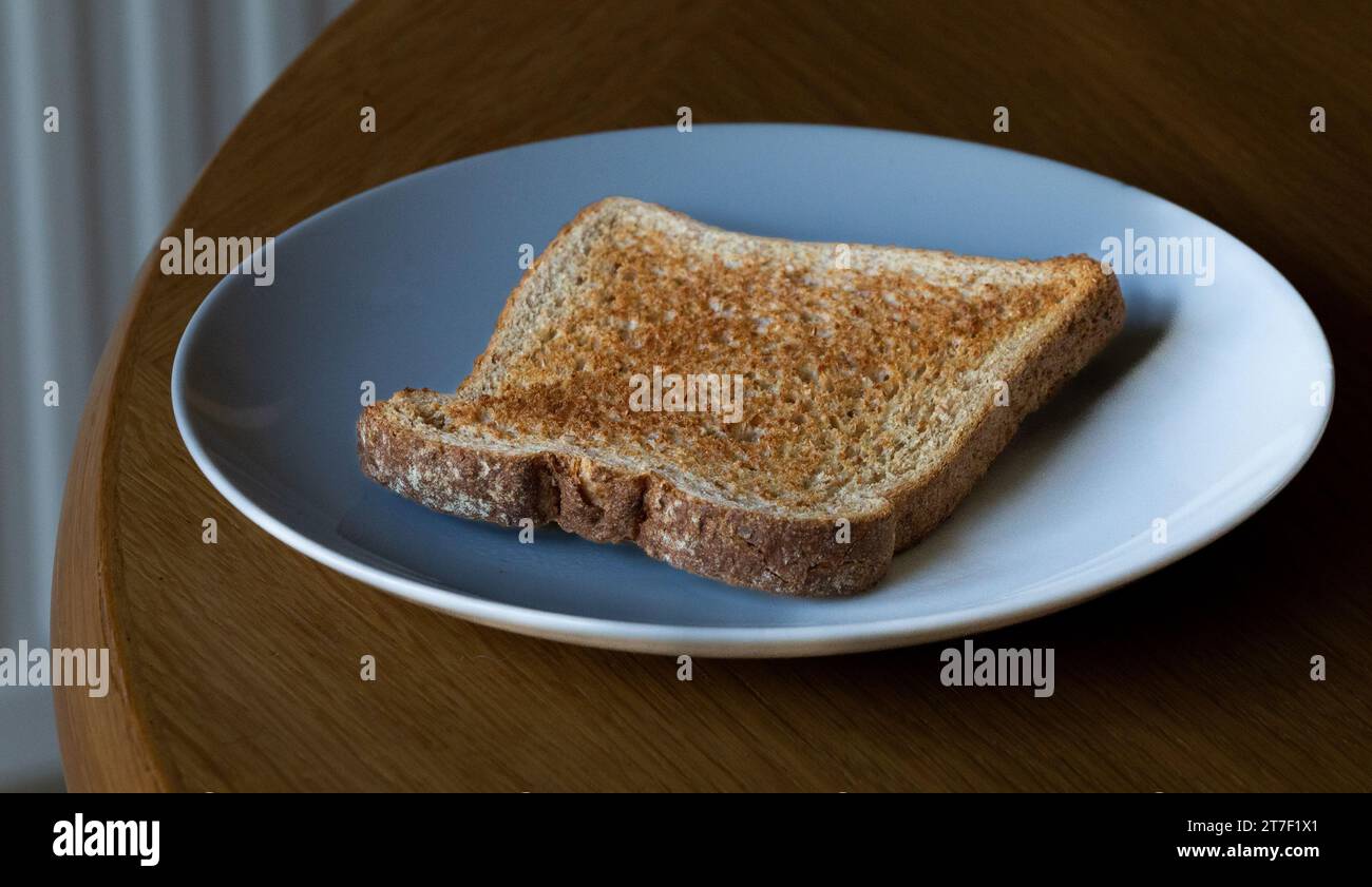 A single slice of wholemeal toast, unbuttered, on a white plate. Stock Photo