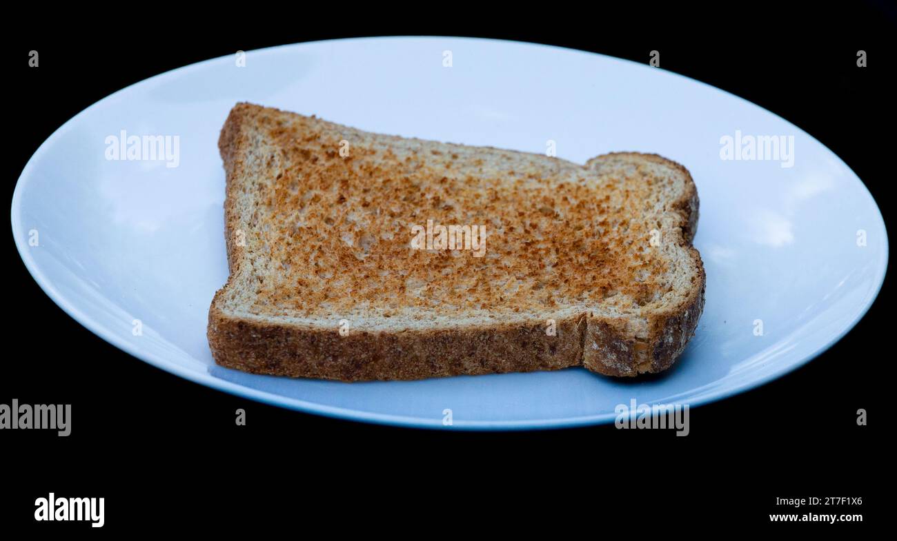 A single slice of wholemeal toast, unbuttered, on a white plate. Stock Photo
