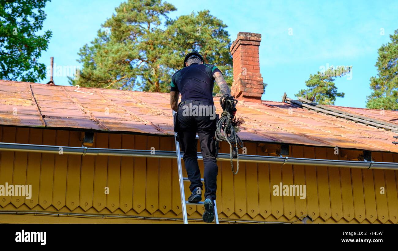 A chimney sweep climbs the stairs on the roof of the house to clean the chimney. Stock Photo