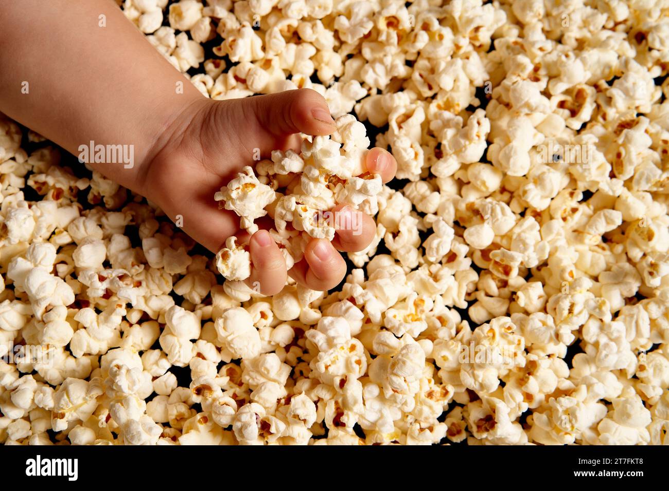 Children's hands are picking up popcorn. Flat lay . The concept of a birthday, party, holiday, home leisure. Copy space for your product. Popcorn texture or background. Stock Photo