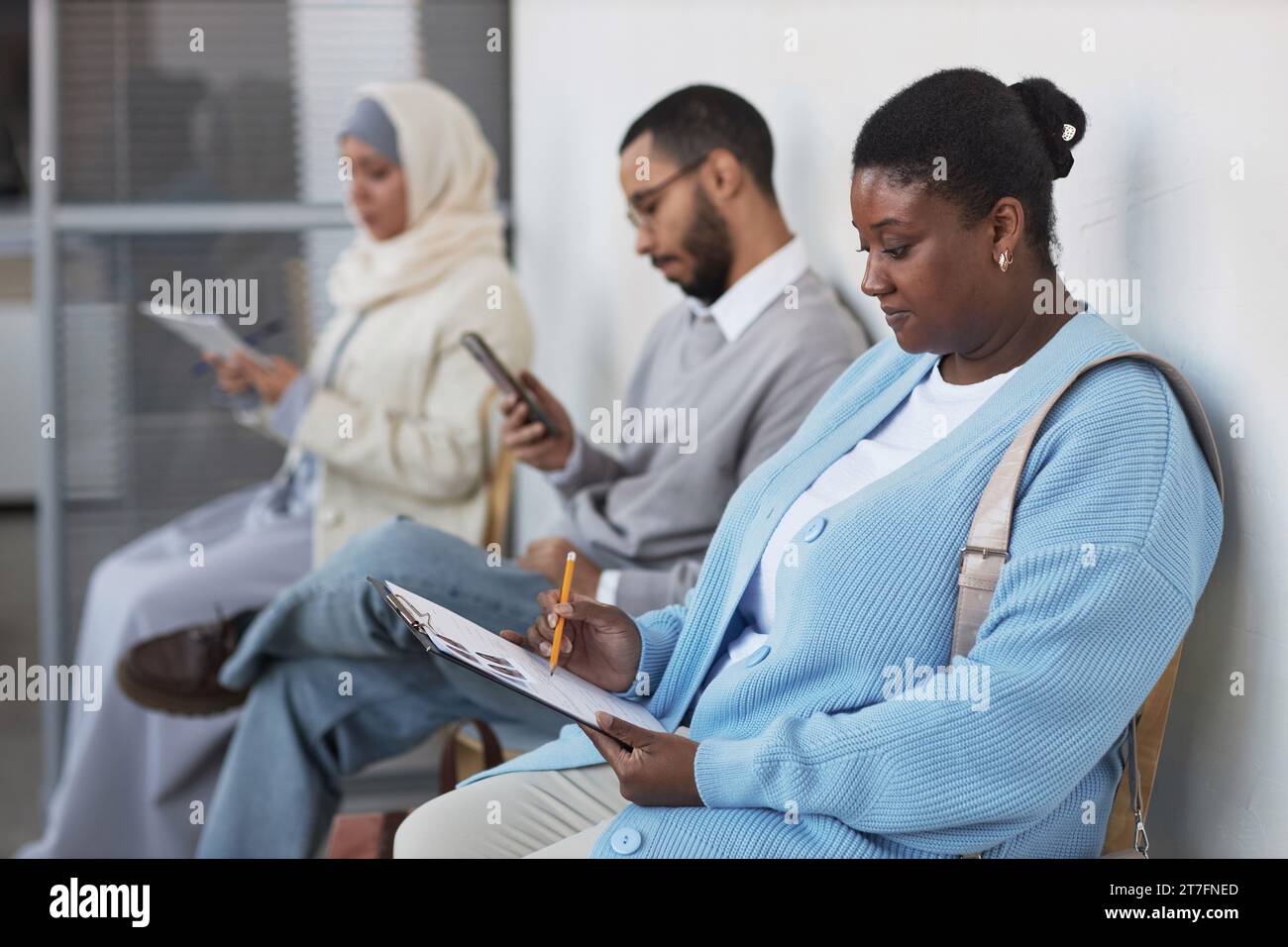 Young African American female applicant pointing at filled form while sitting against other people and checking personal data Stock Photo