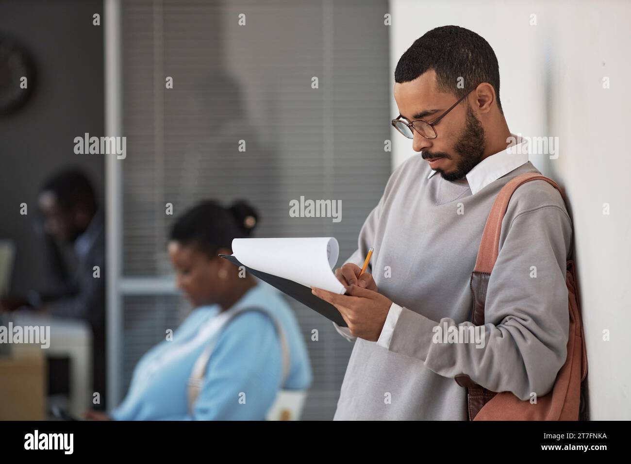 Young male applicant in grey pullover and eyeglasses filling in visa application form and writing down his personal data Stock Photo