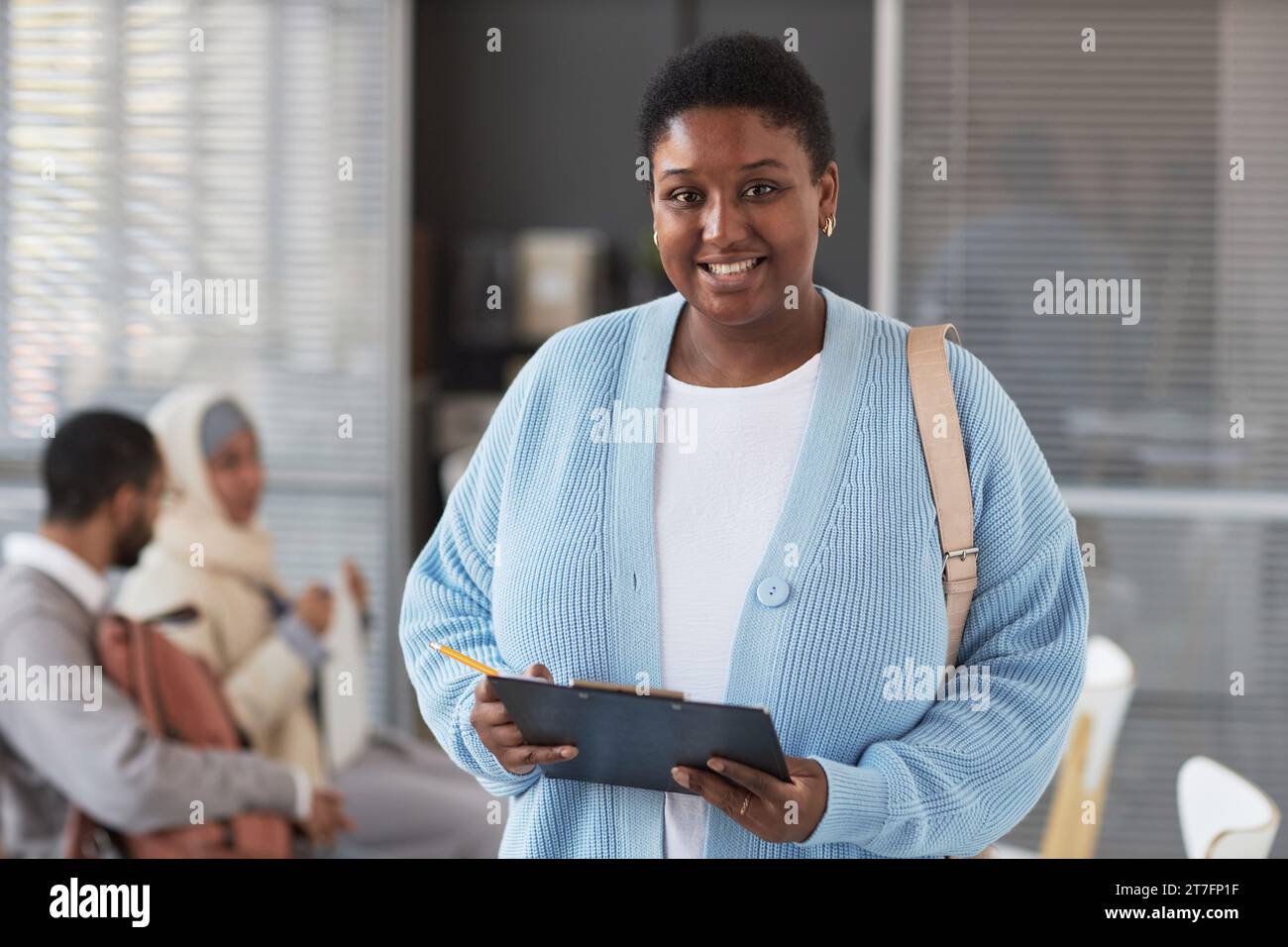 Happy young African American woman in quiet luxury attire standing in front of camera in visa application center and filling in form Stock Photo