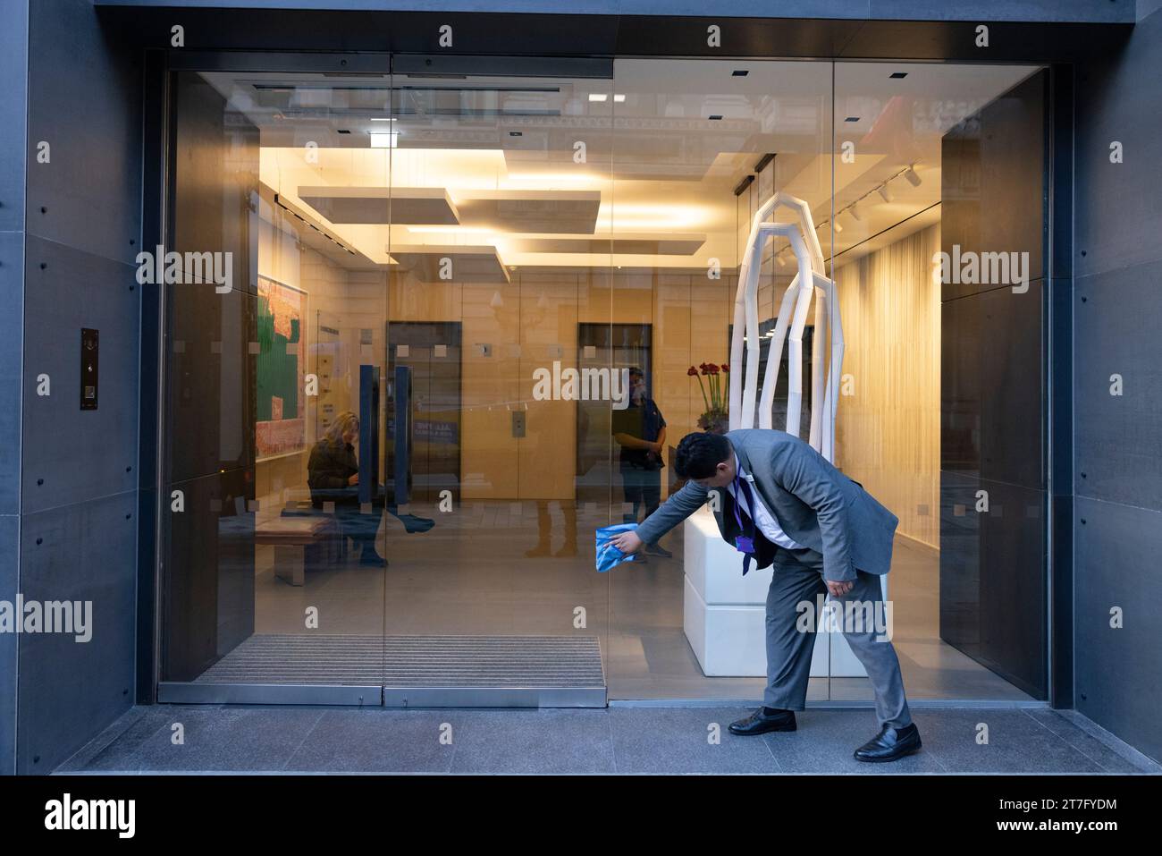 An office worker cleans the windows of a commercial building entrance on New Bond Street, Mayfair, London, UK Stock Photo