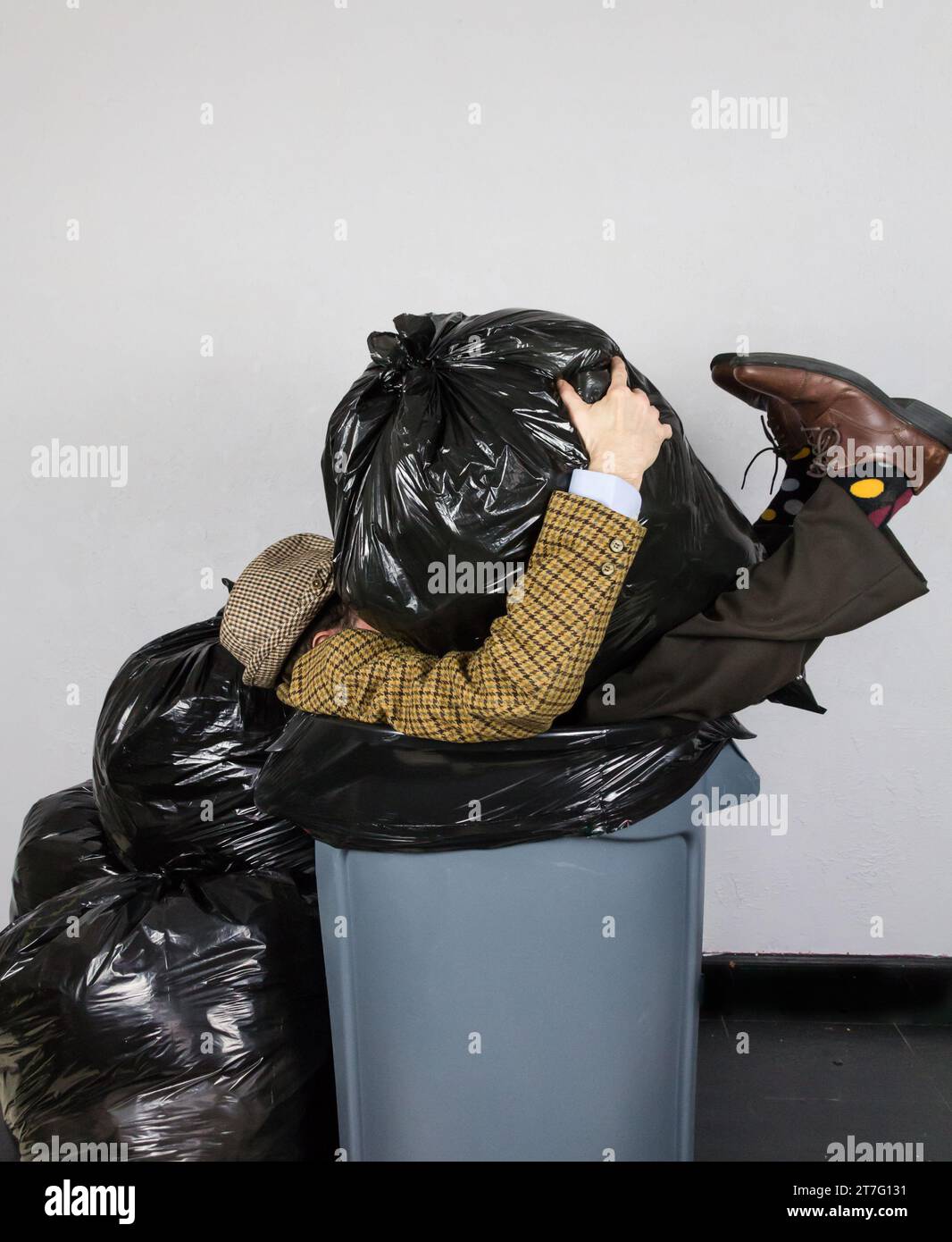Portrait of Man in Suit and Hat and Polk-A-Dot Socks Stuffed in a Garbage Can Surrounded by Trash Bags. Concept of Businessman Thrown Away. Stock Photo