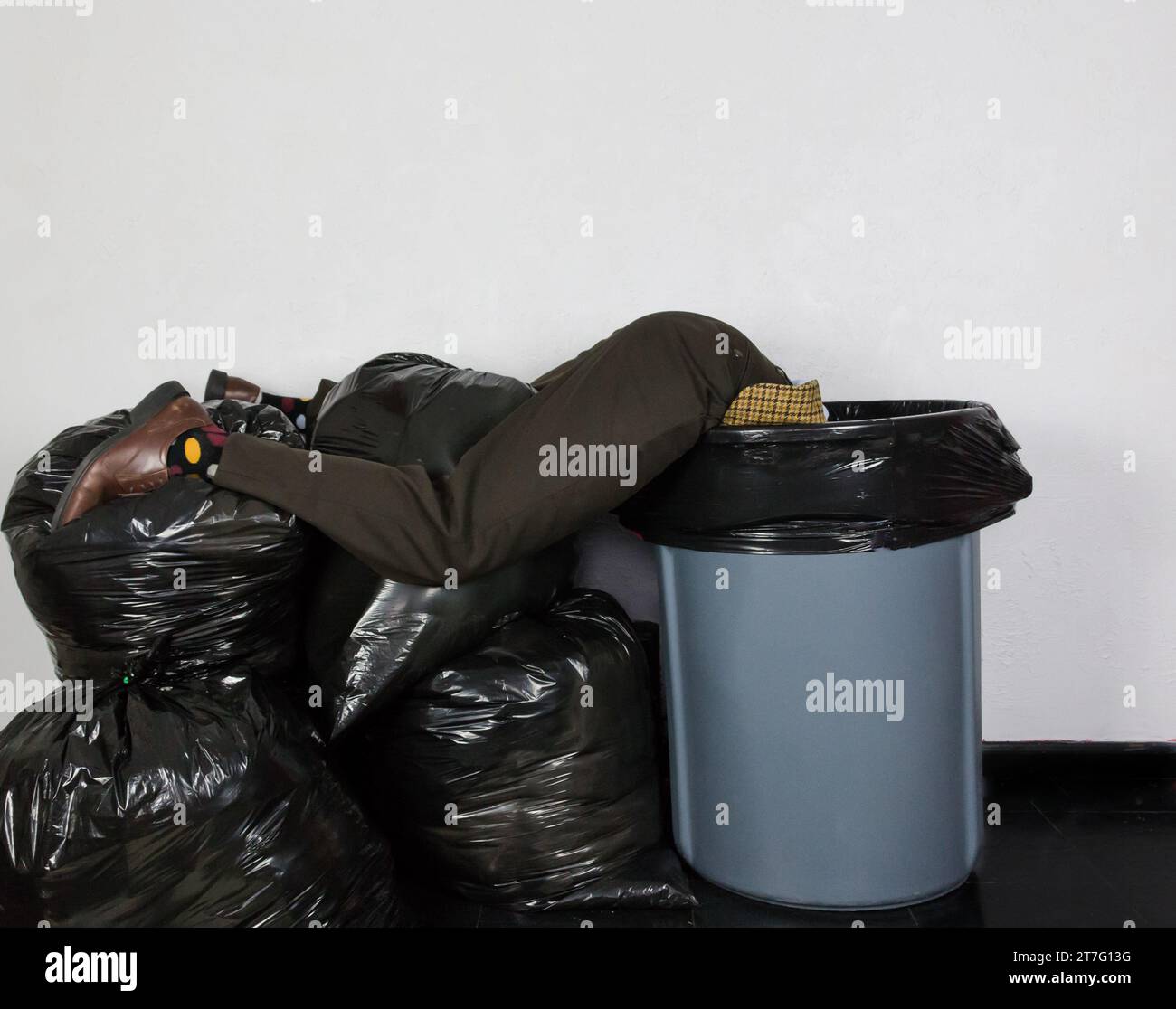 Portrait of Man in Ugly Suit Lying Atop Trash Can and Pile of Trash Bags. Concept of Over a Barrel. Man Thrown Away. Stock Photo
