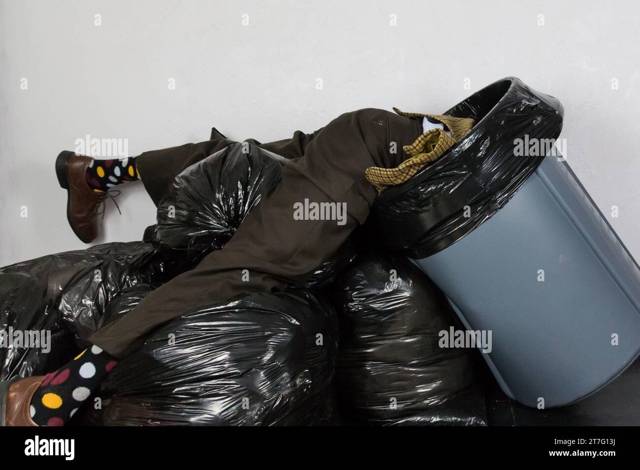 Portrait of Man in Ugly Suit Stuck in Trash Can Atop Pile of Black Garbage Bags. Concept of Over a Barrel. Out of Fashion. Stock Photo