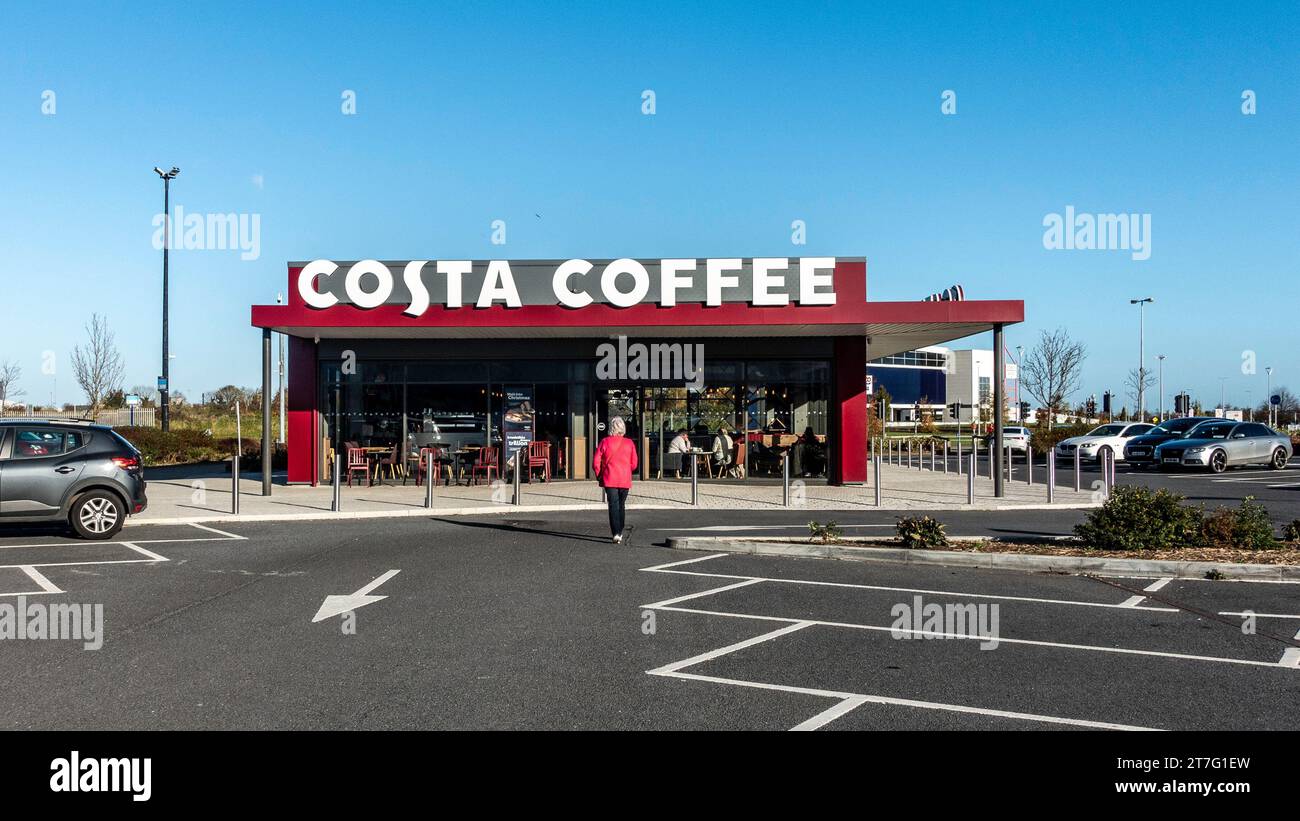Costa Coffee storefront with outdoor seating and clear skies, showcasing the brand's iconic red and white color scheme. Stock Photo
