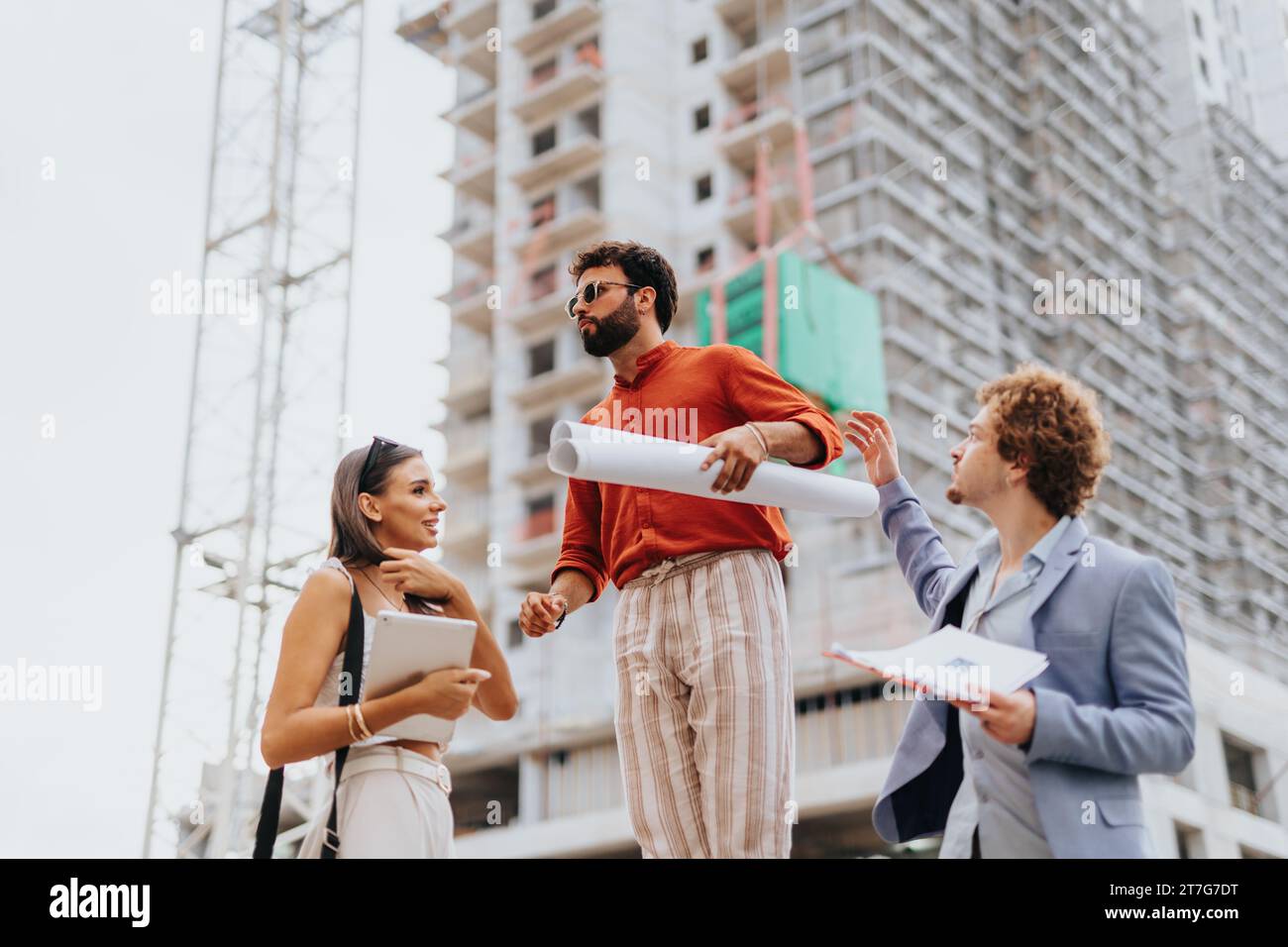 Corporate team analyzing a project blueprint outdoors. Discussing costs, paperwork, and sustainable design. Teamwork for profitable development. Stock Photo