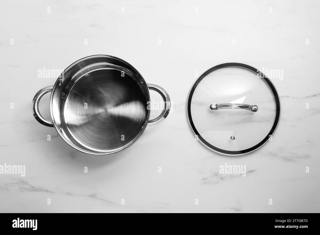 Steel pot and glass lid on white marble table, flat lay Stock Photo