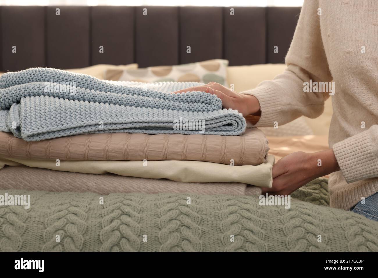 Woman with stack of different folded blankets on bed, closeup. Home textile Stock Photo