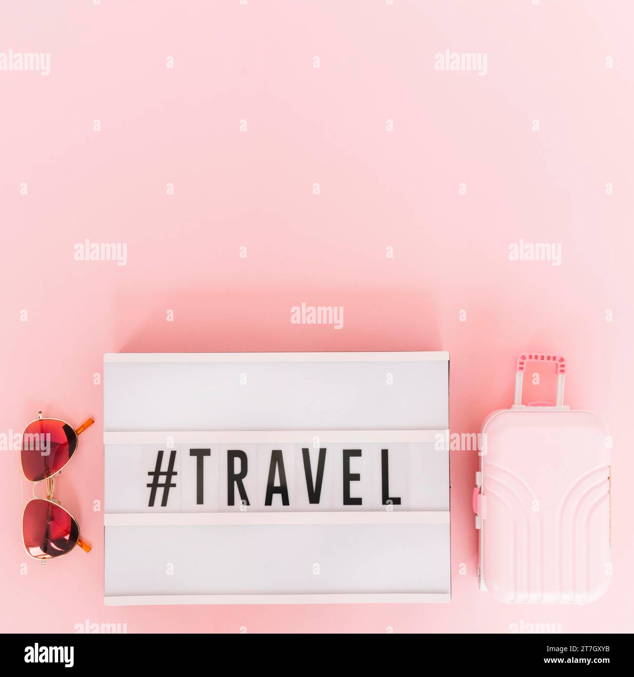 Hashtag with travel text lightbox with sunglasses miniature travel bag pink background Stock Photo