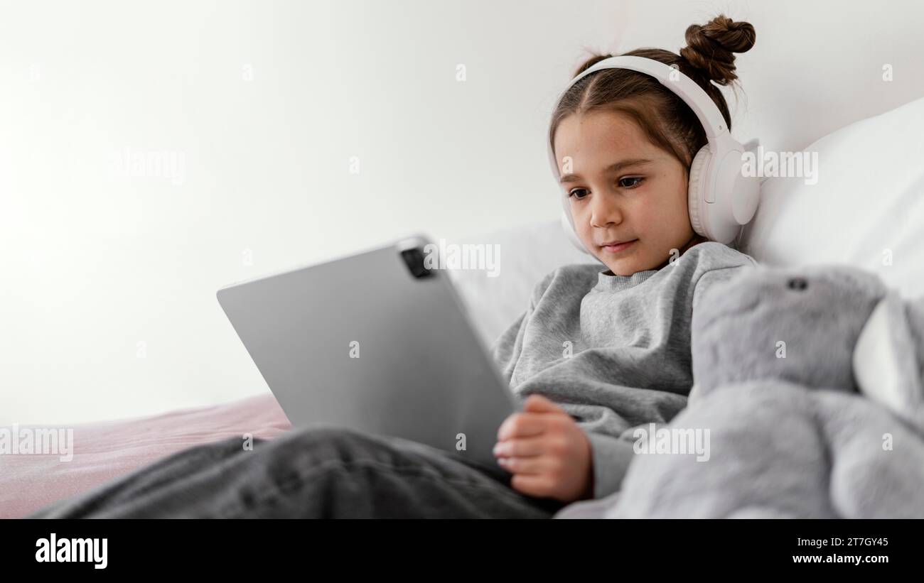 Little girl bed with headphones using tablet 2 Stock Photo