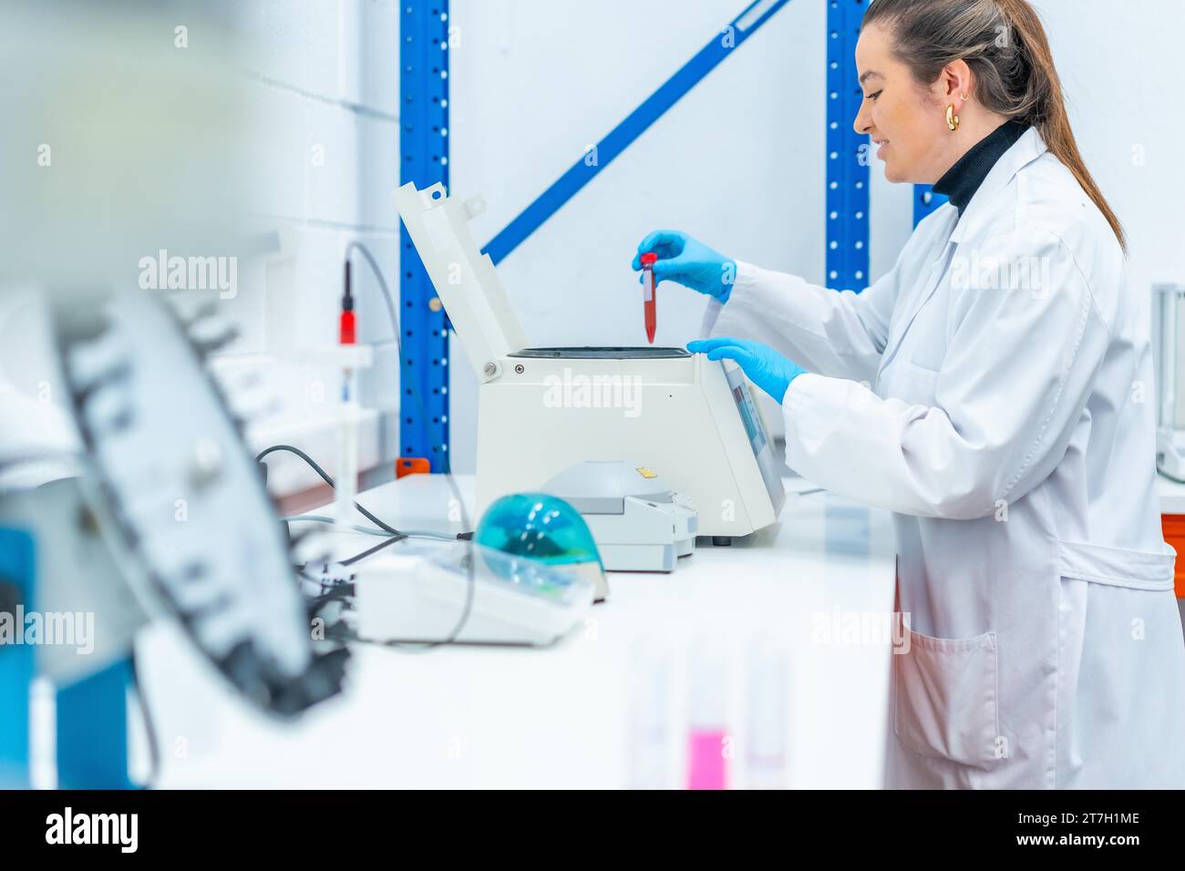 Side view of a smiling scientist placing a blood sample in a centrifuge in a research laboratory Stock Photo