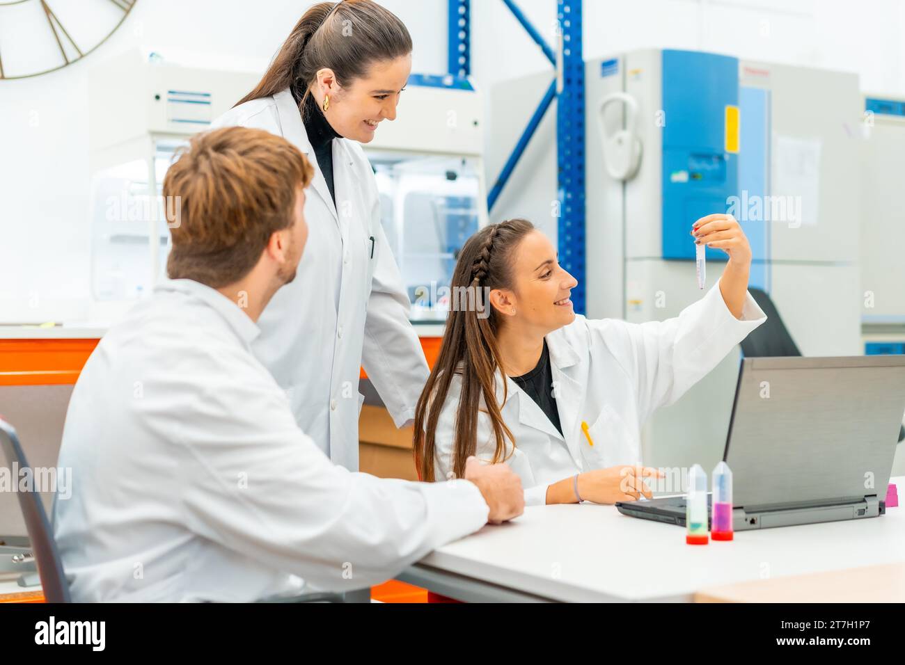 Scientists looking at samples while working with laptop sitting on a table in a lab Stock Photo