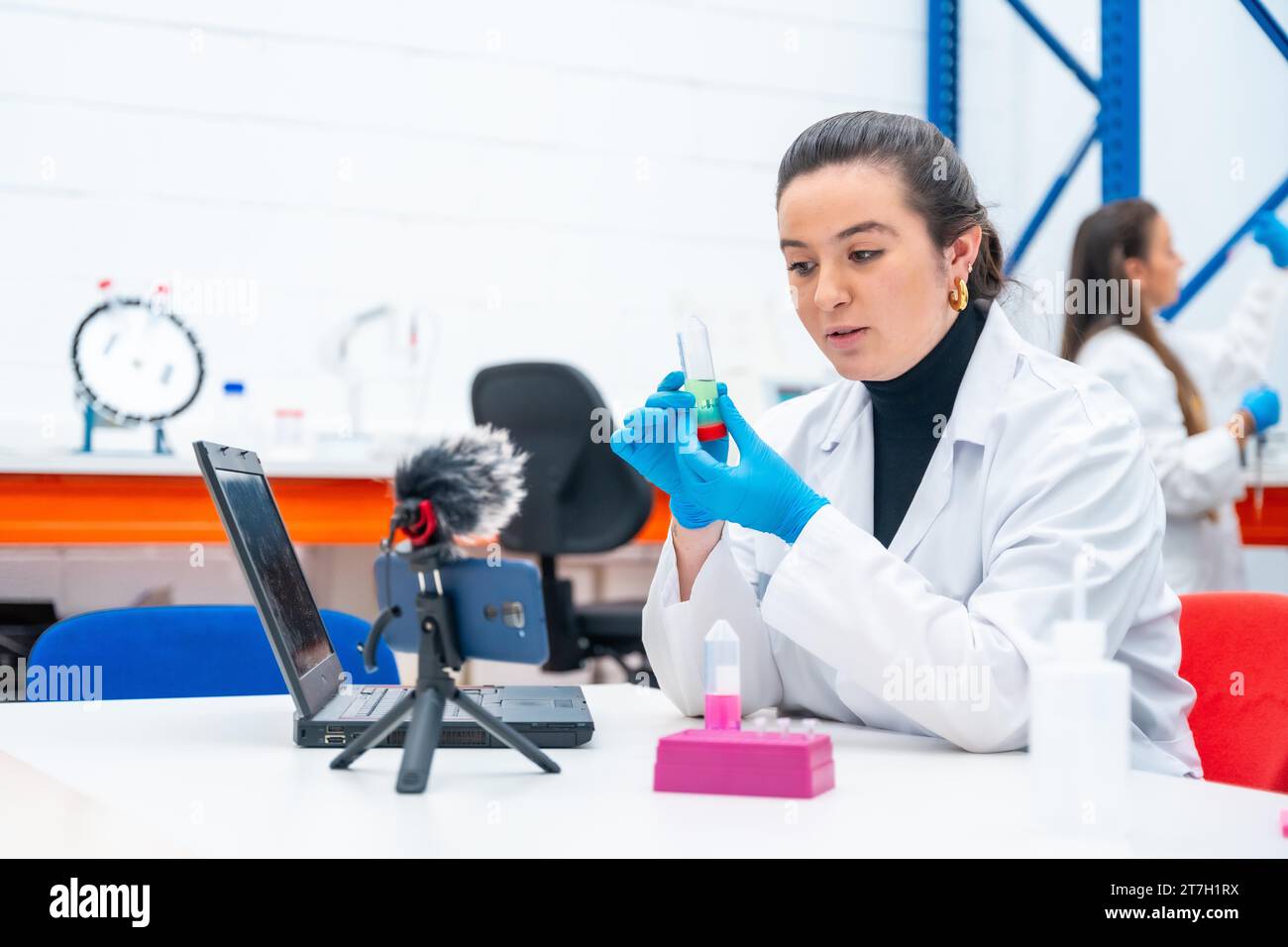 Scientist recording a video tutorial using phone sitting in a research laboratory Stock Photo