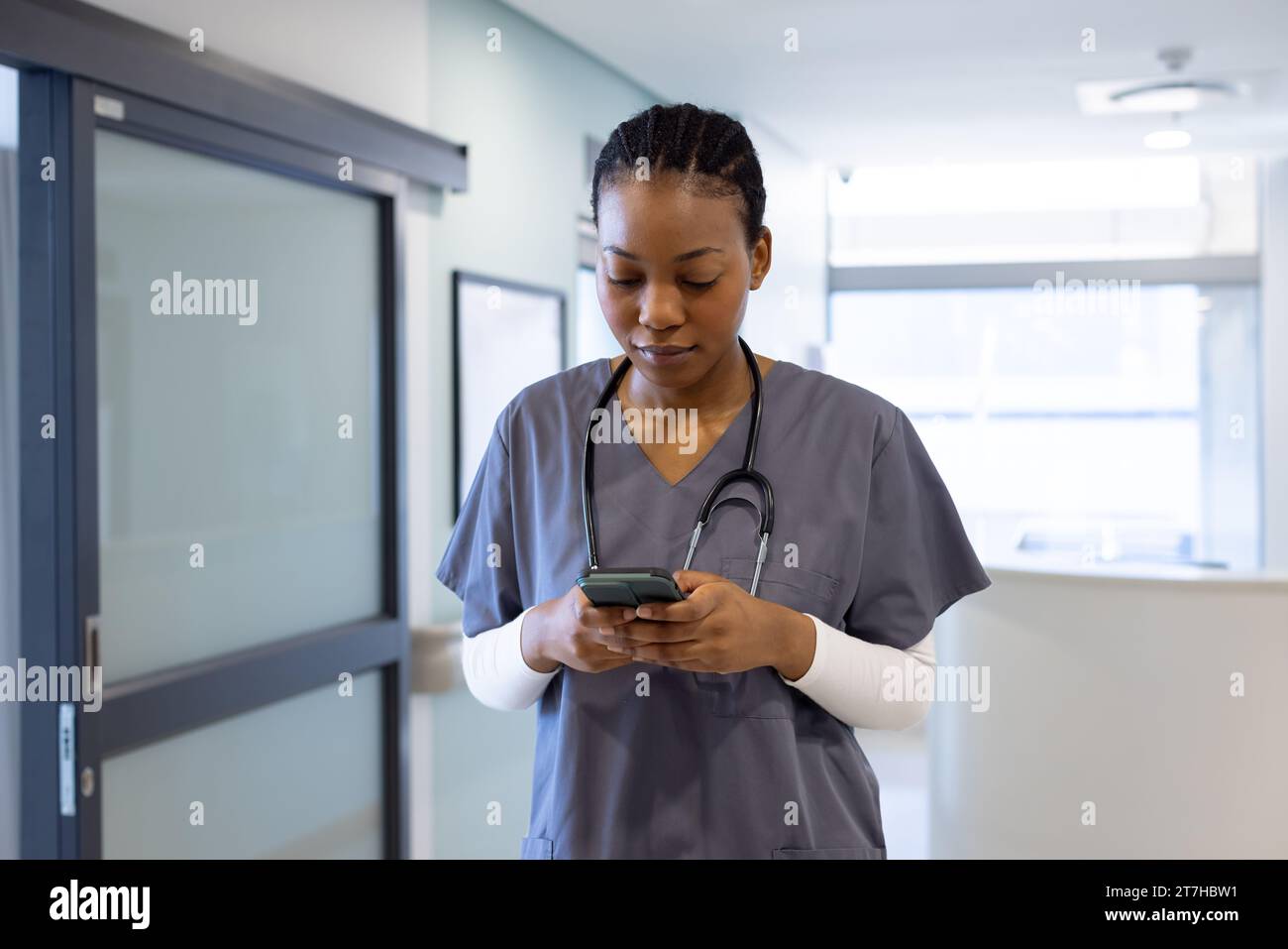 African american female doctor using smartphone in hospital corridor Stock Photo