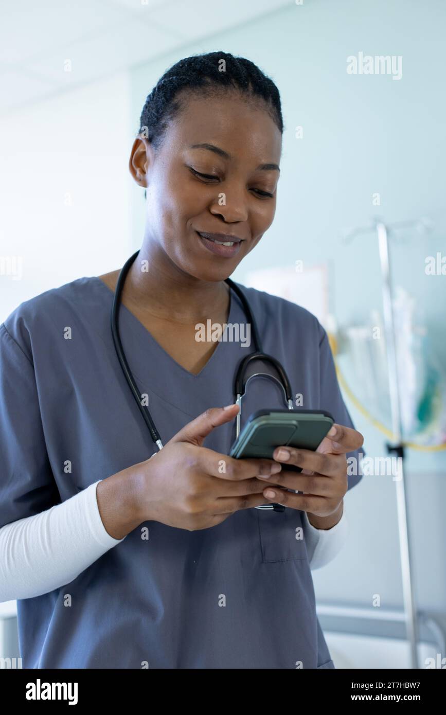 Happy african american female doctor using smartphone in hospital room
