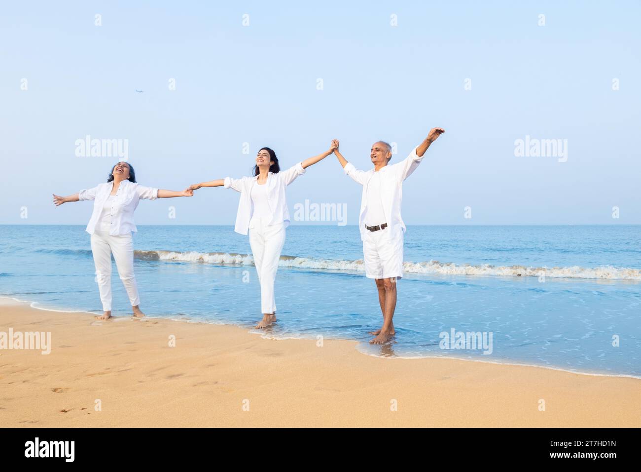 Happy senior indian couple young daughter holding hands enjoying vacation at beach. Stock Photo