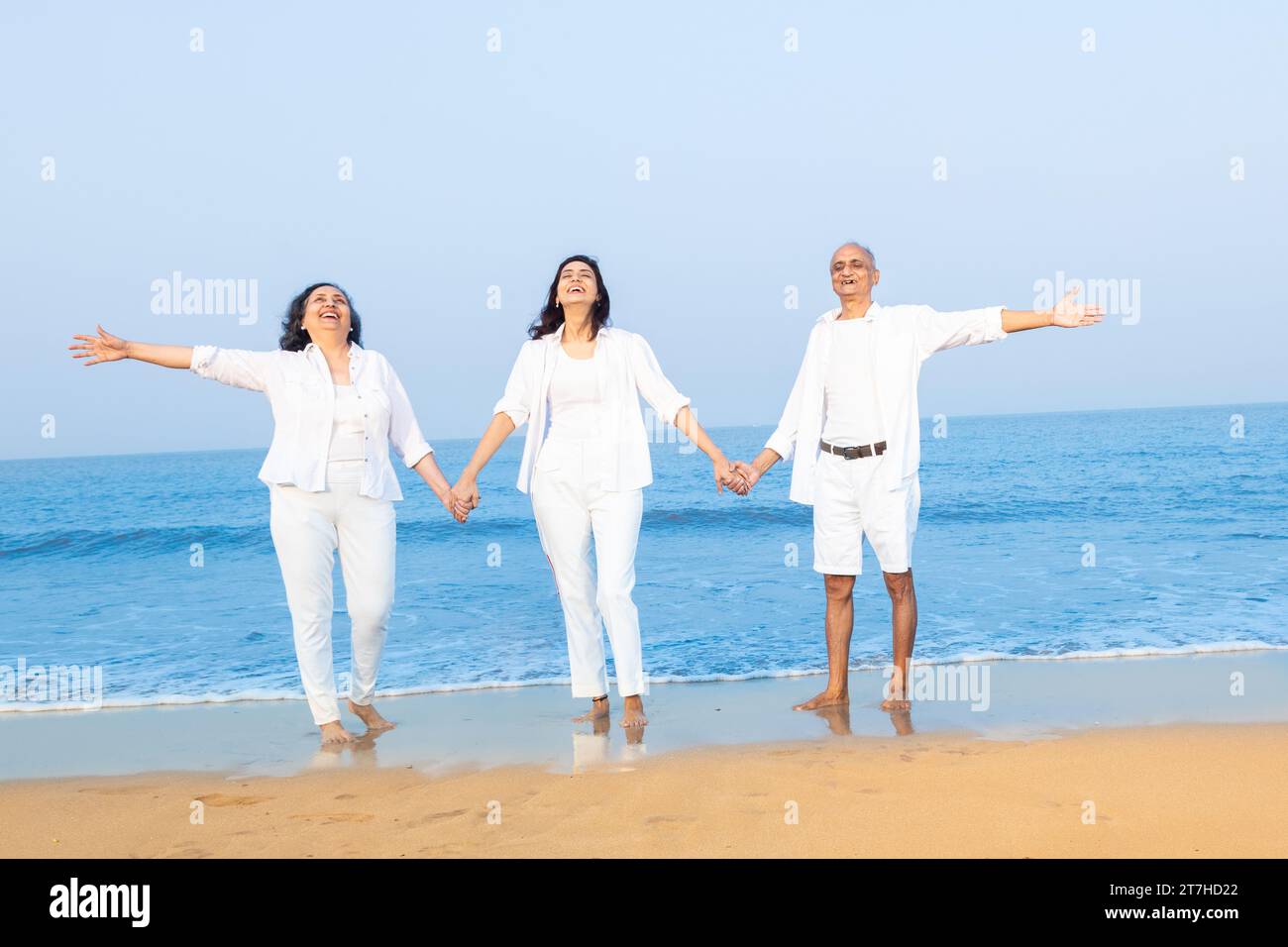 Happy senior indian couple with beautiful young daughter enjoying vacation at beach. Family wearing white cloths having fun together. Stock Photo