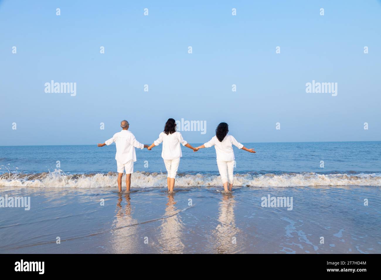 Happy senior indian couple with beautiful young daughter posing and enjoying vacation at beach. Family wearing white cloths having fun together. Stock Photo