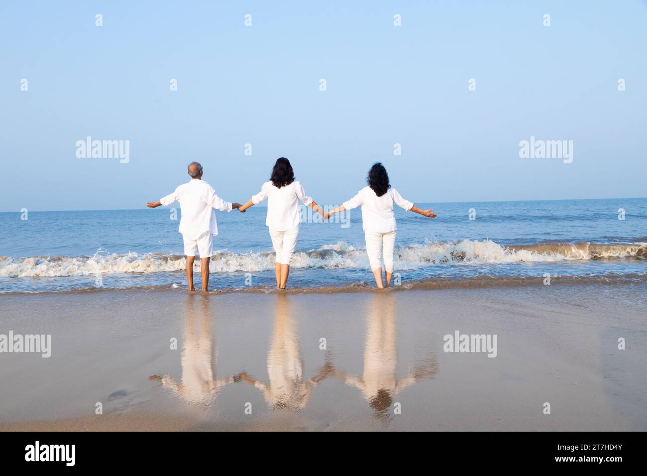 Happy senior indian couple with beautiful young daughter posing and enjoying vacation at beach. Family wearing white cloths having fun together. Stock Photo