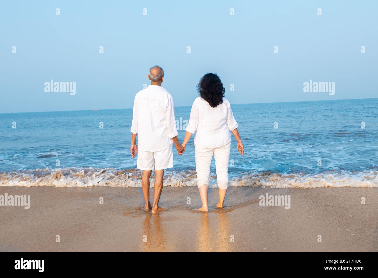 Happy senior indian couple wearing white cloths enjoying summer vacation, holiday at beach looking at sea. Copy space Stock Photo