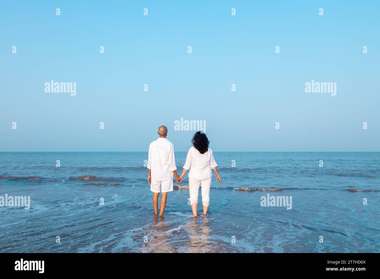 Happy senior indian couple wearing white cloths enjoying summer vacation, holiday at beach looking at sea. Copy space Stock Photo
