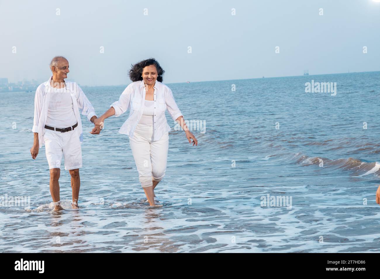 Happy carefree senior indian couple walking together and enjoying summer vacation, holiday at beach. Retirement life. Stock Photo