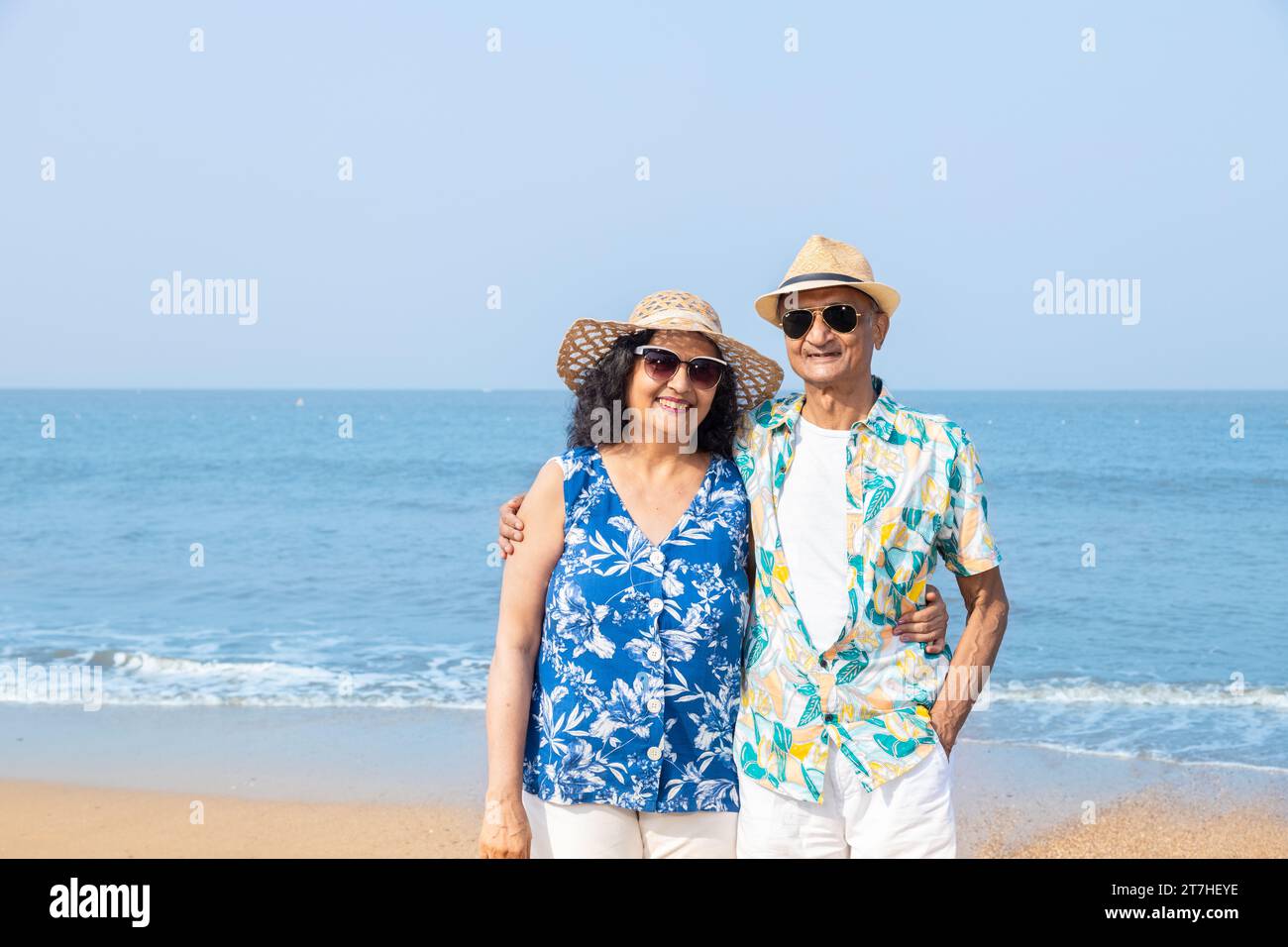Happy senior indian couple wearing hat and sunglasses enjoying vacation at beach. Copy space. Stock Photo
