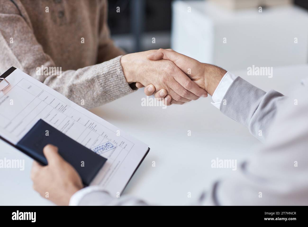 Handshake of mature female manager of visa application center and young male applicant holding passport and approved form Stock Photo
