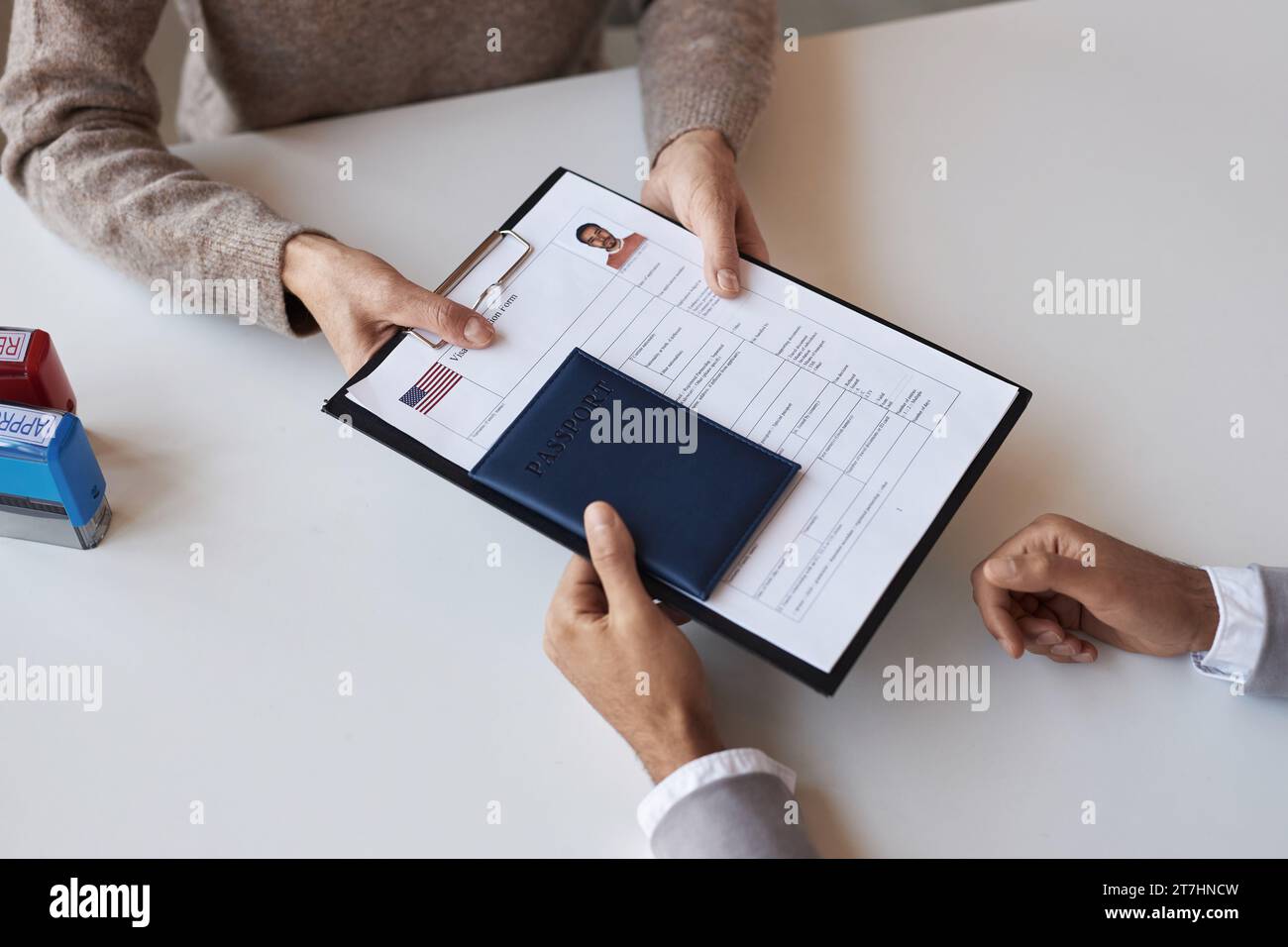 Above angle of filled form for visa request and passport being passed by male applicant to mature female manager of application center Stock Photo