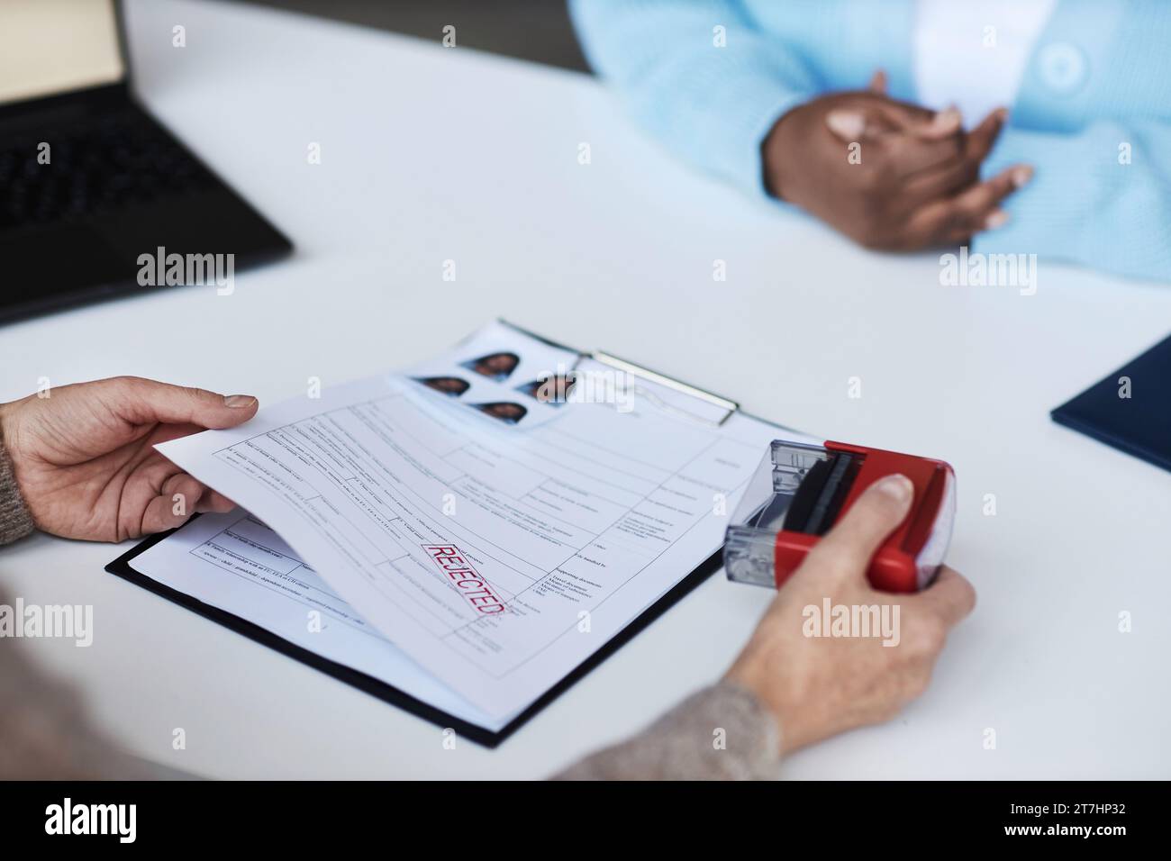 Hands of female manager of visa application center putting rejected stamp on filled form of African American applicant sitting in front of her Stock Photo