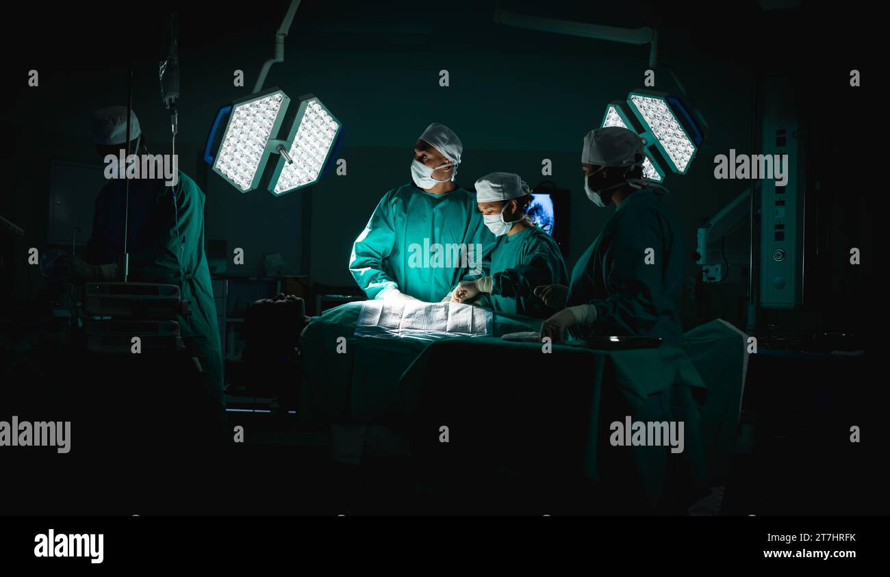Diverse surgeons wearing surgical gowns operating on patient in operating theatre at hospital Stock Photo
