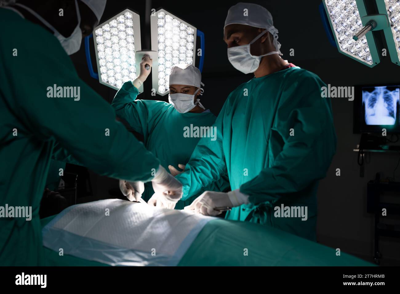 Diverse surgeons wearing surgical gowns operating on patient in operating theatre at hospital Stock Photo