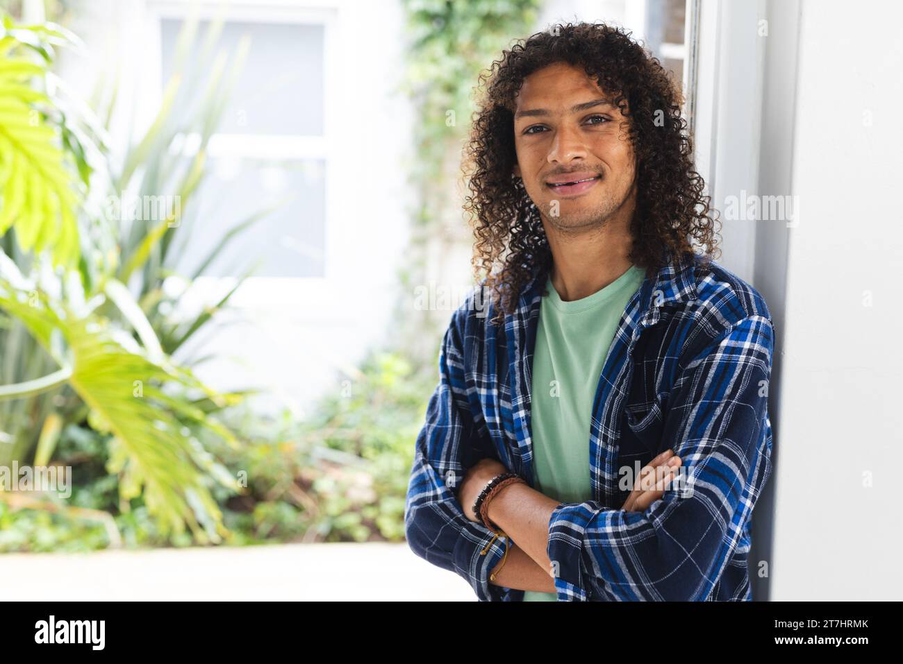 Happy biracial man with long dark curly hair smiling in sunny living room at home Stock Photo