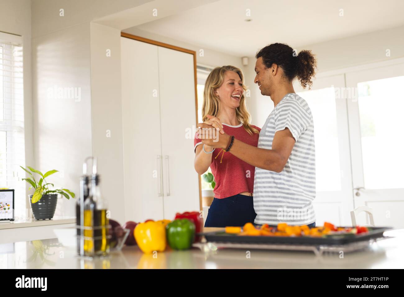 Happy diverse couple dancing at counter with vegetables in sunny