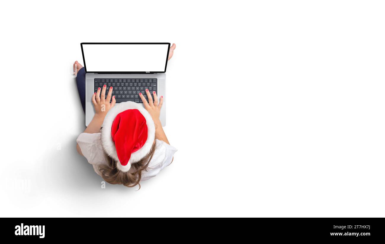 Top view of girl in Christmas hat works on laptop with isolated screen for mockup. Copy space Stock Photo